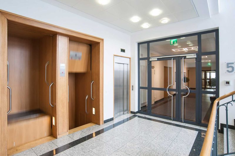 Aufzugsbereich mit holzverkleideten Wänden und Glastür im 5. Obergeschoss