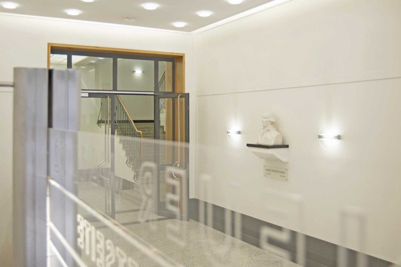 Heller Eingangsbereich mit Glasbrüstung und Büste an der Wand